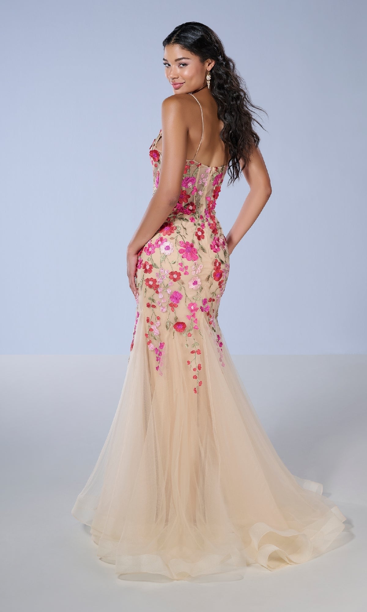 A woman poses in the Tiffany 16148 Long Prom Dress, a floor-length nude tulle gown with pink floral embroidery, lace appliqué, a fitted bodice, and thin straps, set against a plain light background.